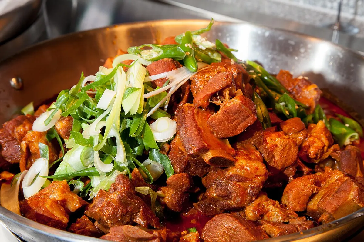 넓은 스테인리스 팬에 담긴 매운 돼지갈비찜. 빨간 양념의 갈비 위에 어슷 썬 대파와 청고추가 수북이 올라가 있는 모습