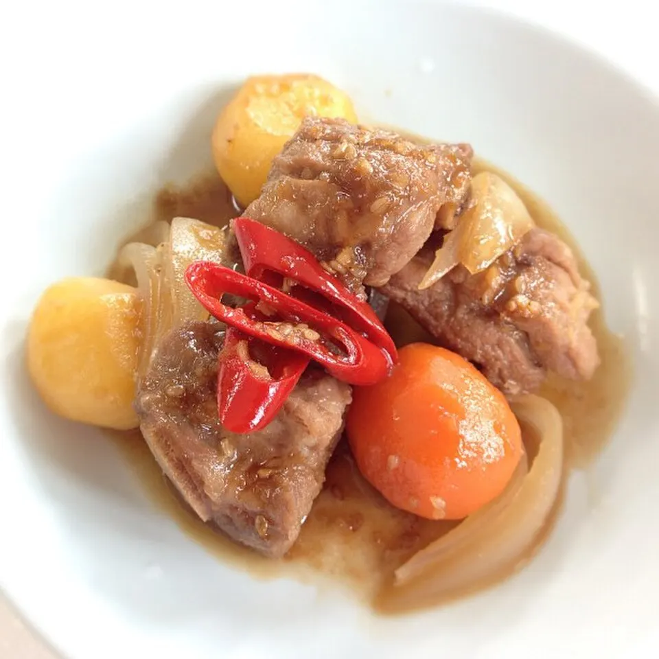 흰 그릇에 담긴 돼지갈비찜. 간장 양념이 밴 고기와 감자, 당근, 양파 위에 붉은 고추가 올라가 있는 모습