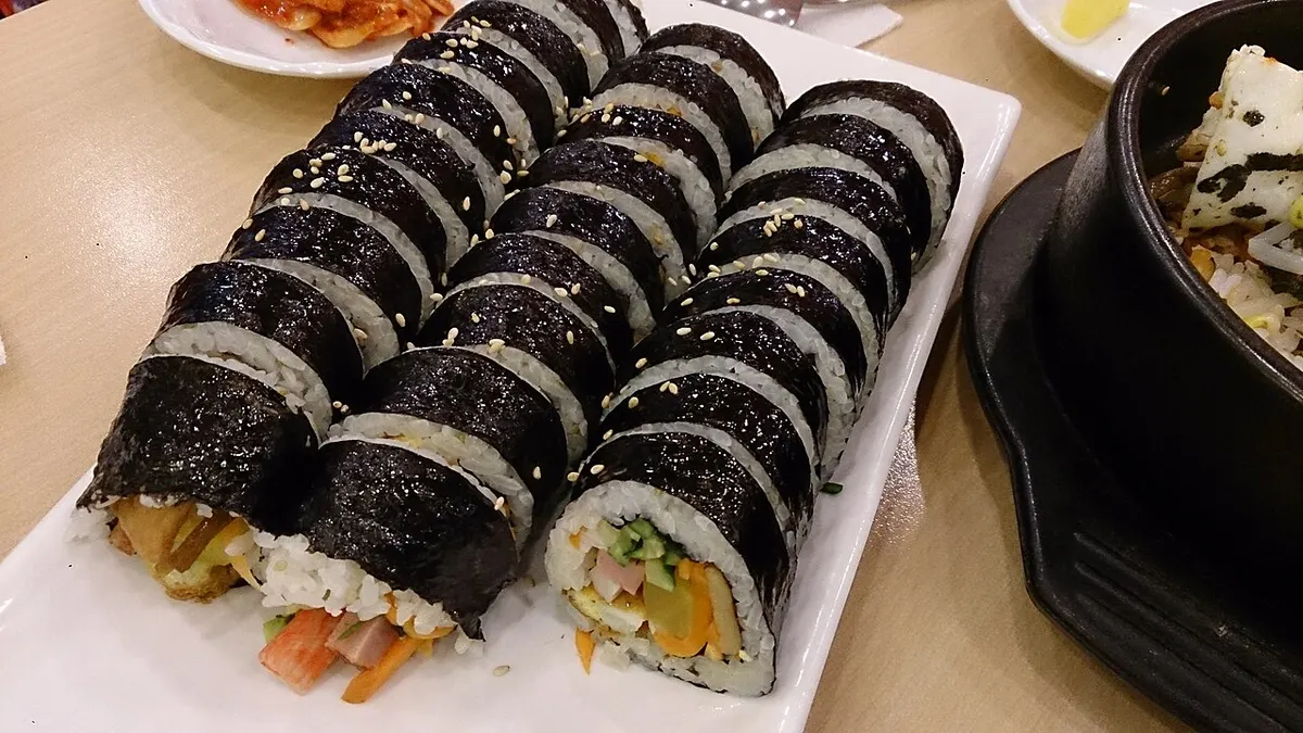 접시에 세 줄로 가지런히 썰어 놓은 김밥과 통깨 고명