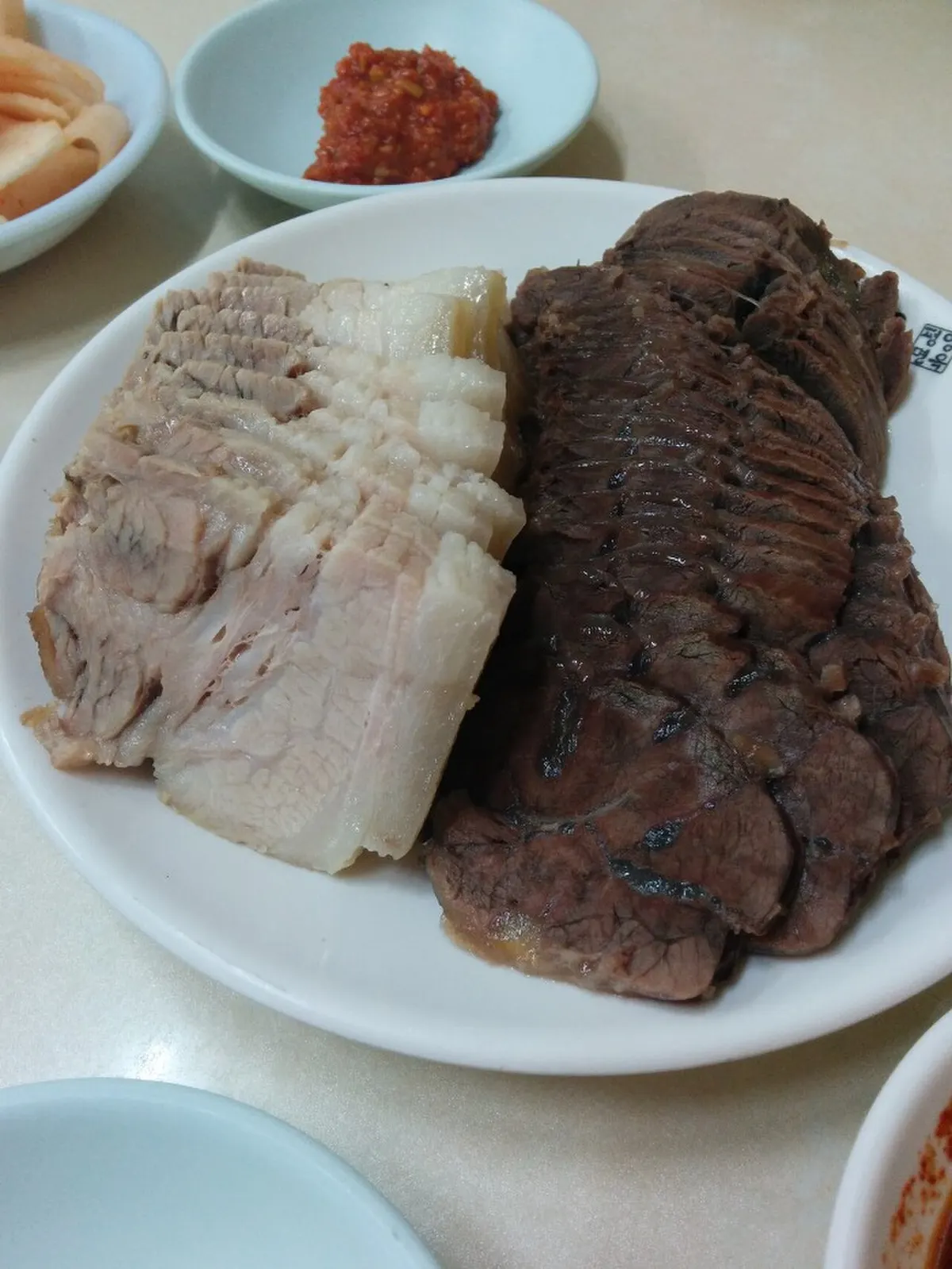 접시 왼쪽에 지방층이 살아 있는 돼지고기 수육, 오른쪽에 얇게 썬 소고기 편육이 담긴 모습