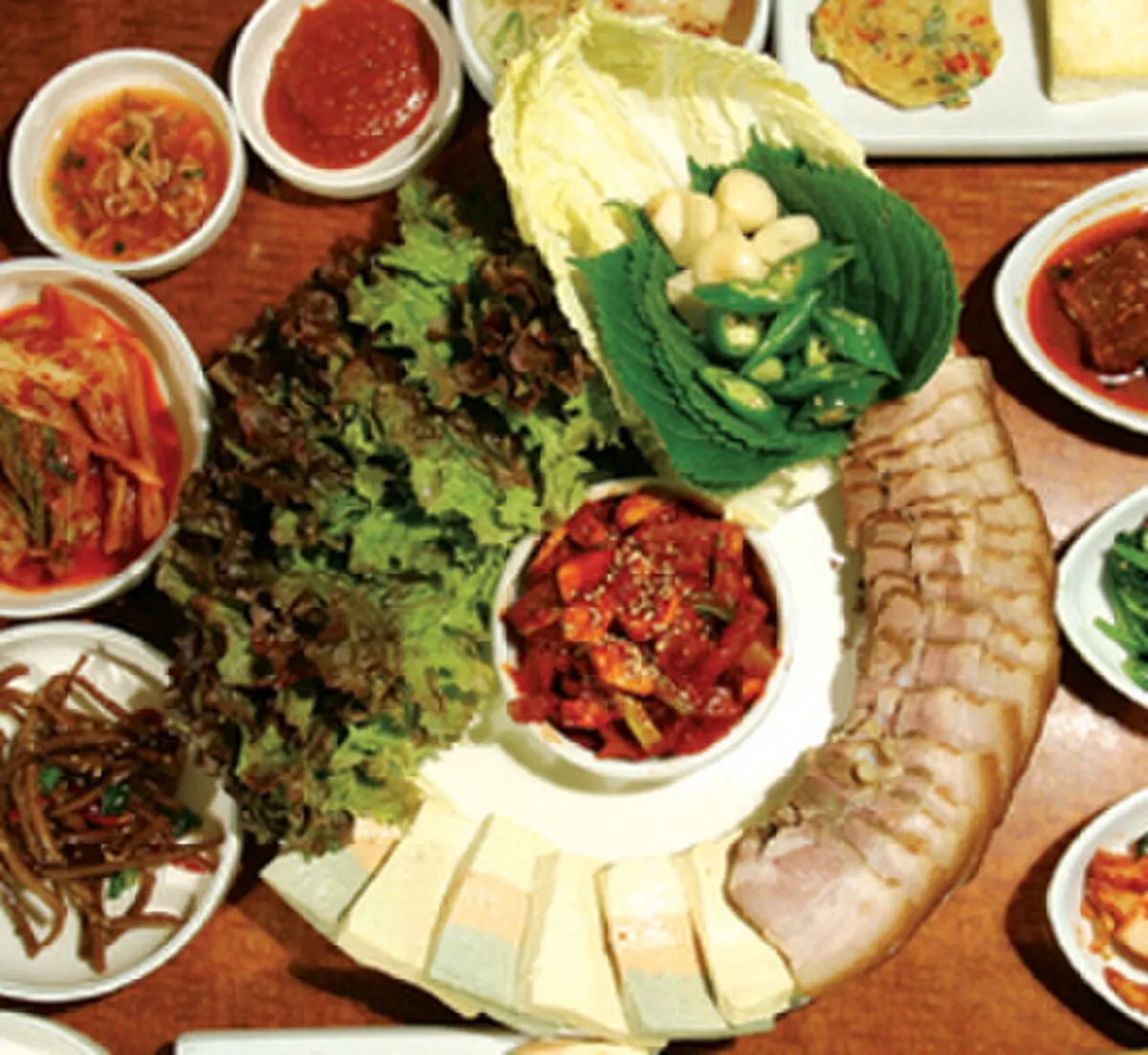 배추잎과 깻잎, 마늘, 고추, 무김치, 두부와 함께 둥글게 차려 낸 보쌈 한 상