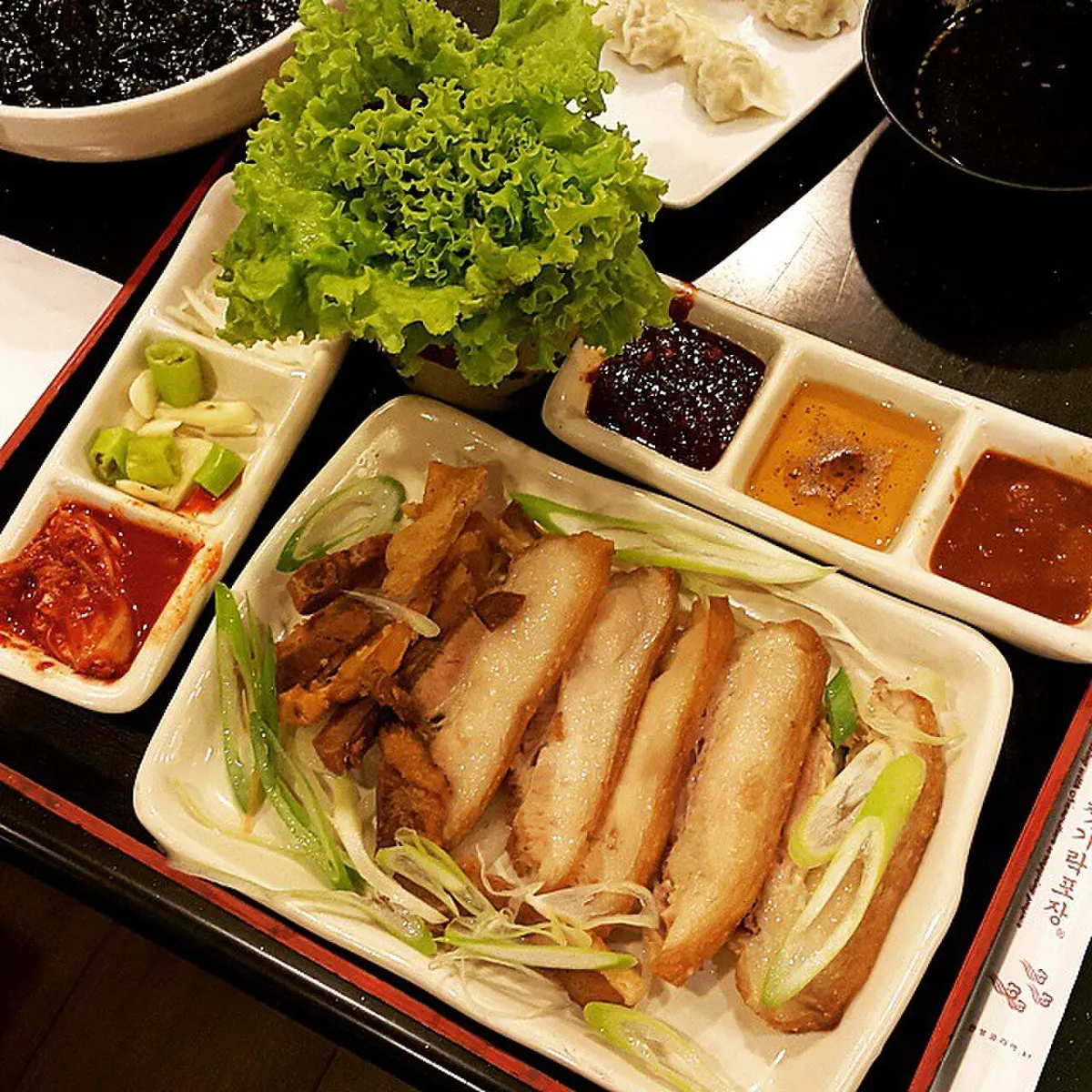 썰어 낸 보쌈 수육과 상추, 파채, 새우젓과 양념장 종지가 함께 차려진 상