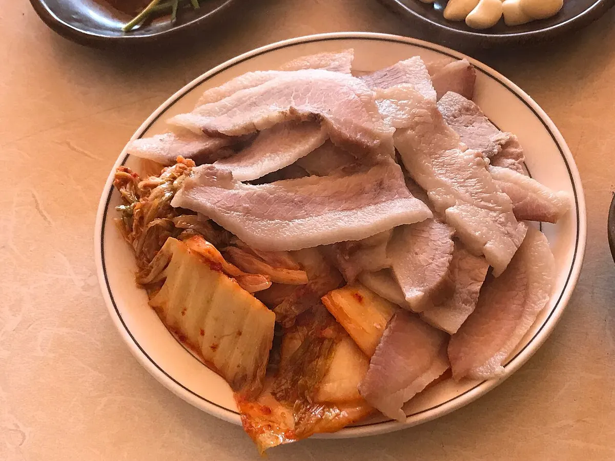 접시에 배추김치와 함께 수북하게 담긴 얇게 썬 돼지고기 수육