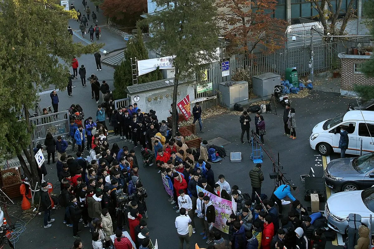 수능 시험일 아침, 시험장 교문 앞에 수험생과 응원 나온 사람들이 모여 있는 모습